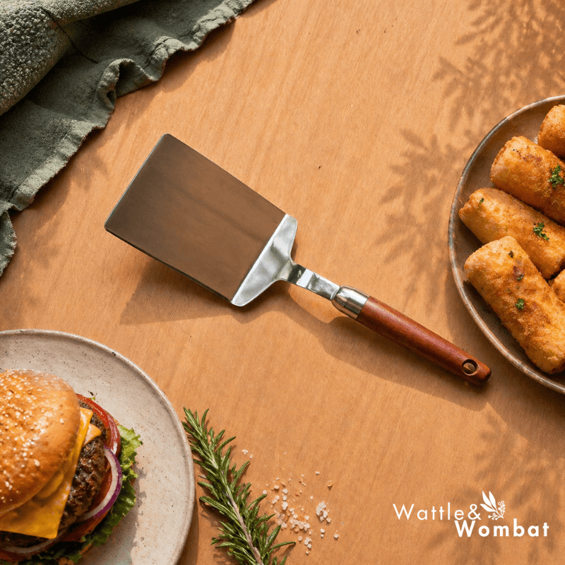 Spatula on a wooden surface with a burger and fries, featuring the Wattle & Wombat logo.